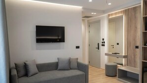 Una habitación moderna con un sofá gris, un televisor de pantalla plana montado en la pared, una puerta de madera y un pequeño taburete.