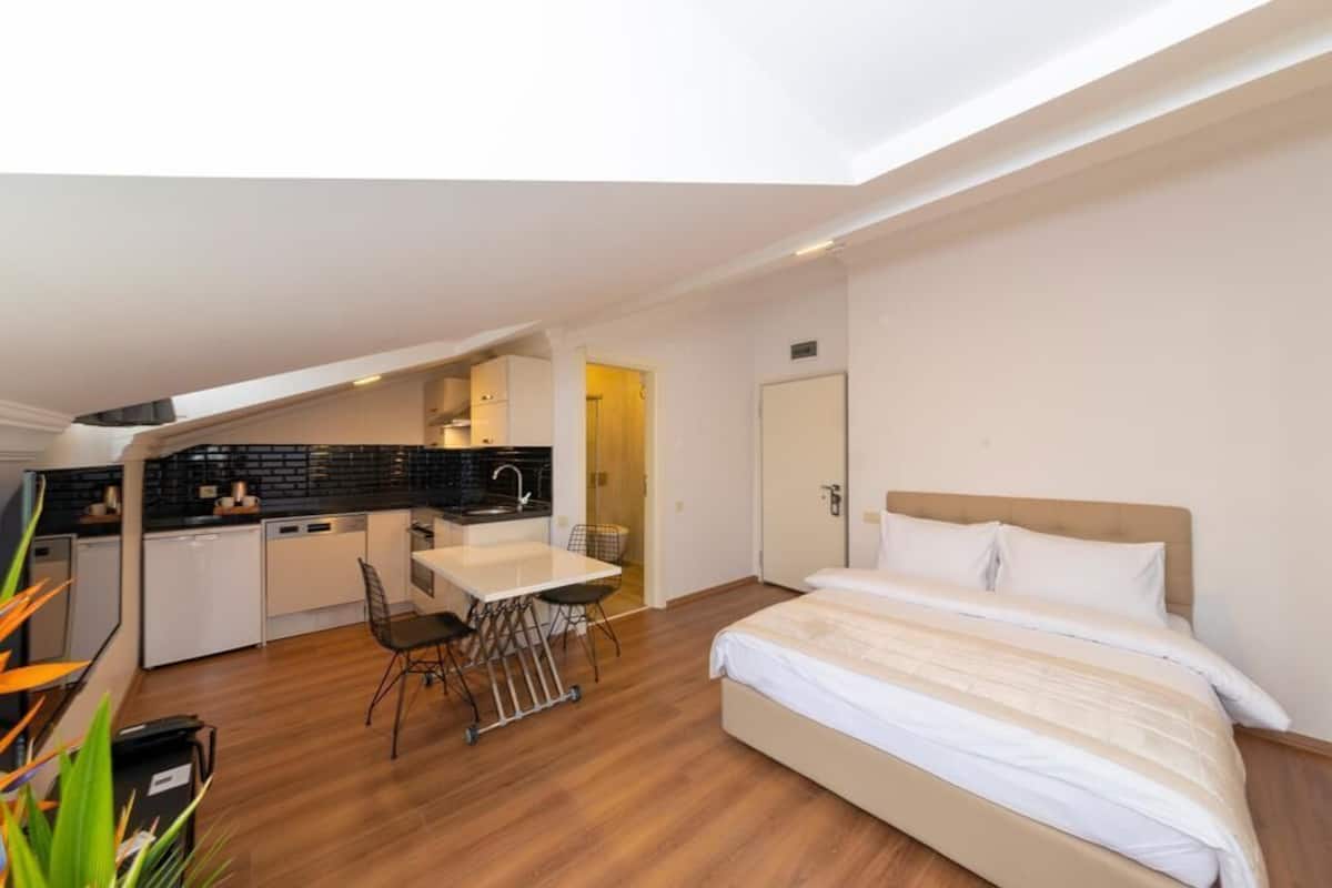 A compact hotel room with a kitchenette, a bed, and a dining area.