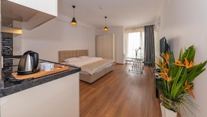 Moderni hotellihuone, jossa on sänky, pieni keittiö, ruokailutila ja suuri ikkuna.