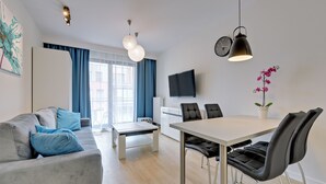 Una sala de estar moderna con sofá, mesa de centro, mesa de comedor y sillas. Hay un televisor montado en la pared y un reloj.