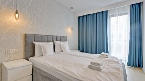 Una habitación de hotel moderna con una cama grande, una mesita de noche y una mesita auxiliar.