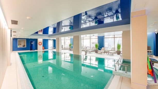 Una piscina interior con agua cristalina, rodeada de sillones de descanso y una terraza con sol.