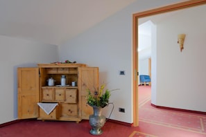 A room with a wooden cabinet, a metal vase with plants, and a blue chair. - Hotel Haus an der Luck (Barbiano)