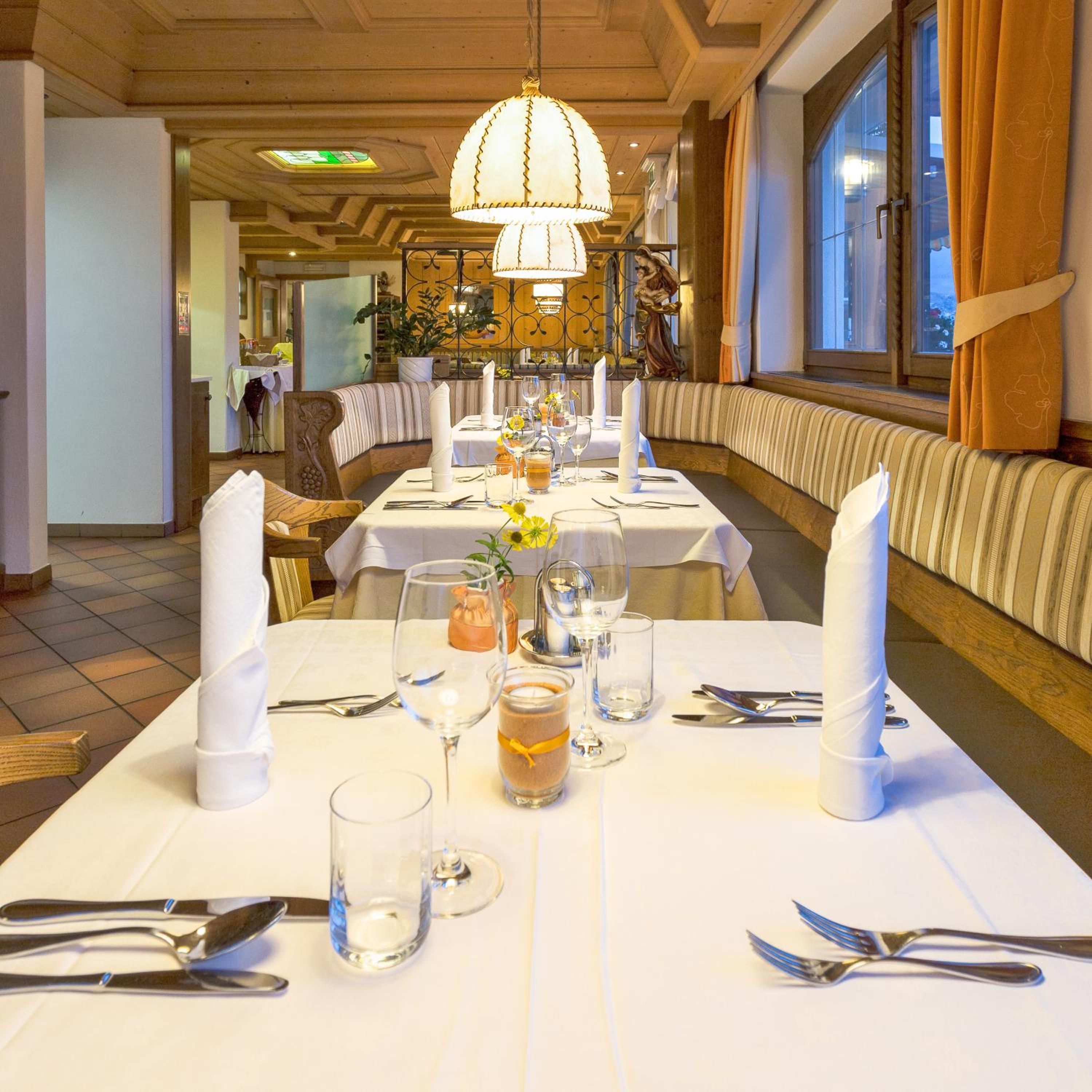A restaurant with a long table set for dining, a chandelier, and a view through the window.