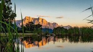 A calm lake with reflections of a mountain range and surrounding vegetation. - Hotel Haus an der Luck (Barbiano)