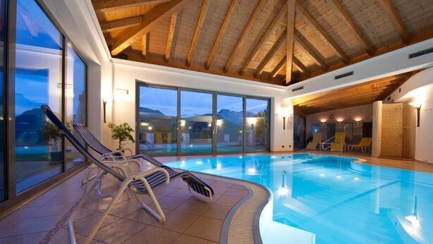 An indoor swimming pool with a wooden ceiling and large windows. - Hotel Haus an der Luck (Barbiano)