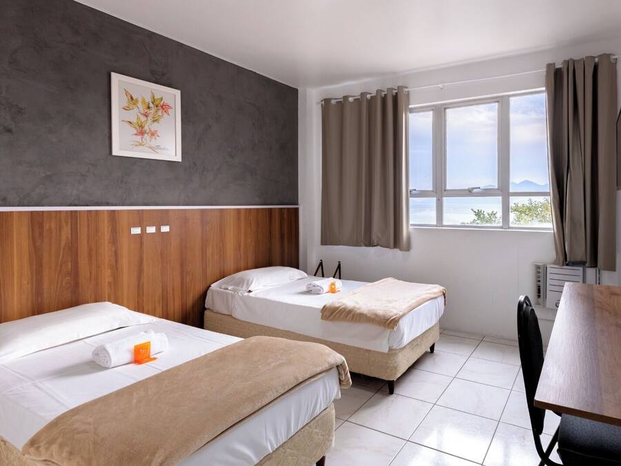 Habitación de hotel con dos camas, cabecera de madera, ventana con cortinas, televisor de pantalla plana y una mesa.