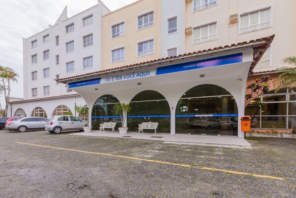 Un hôtel doté d’une entrée abritée, de nombreuses fenêtres et d’un parking où sont garées des voitures.
