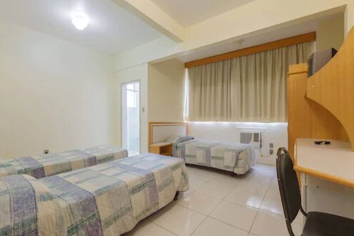A hotel room with two beds, a desk, a chair, and a window with curtains.