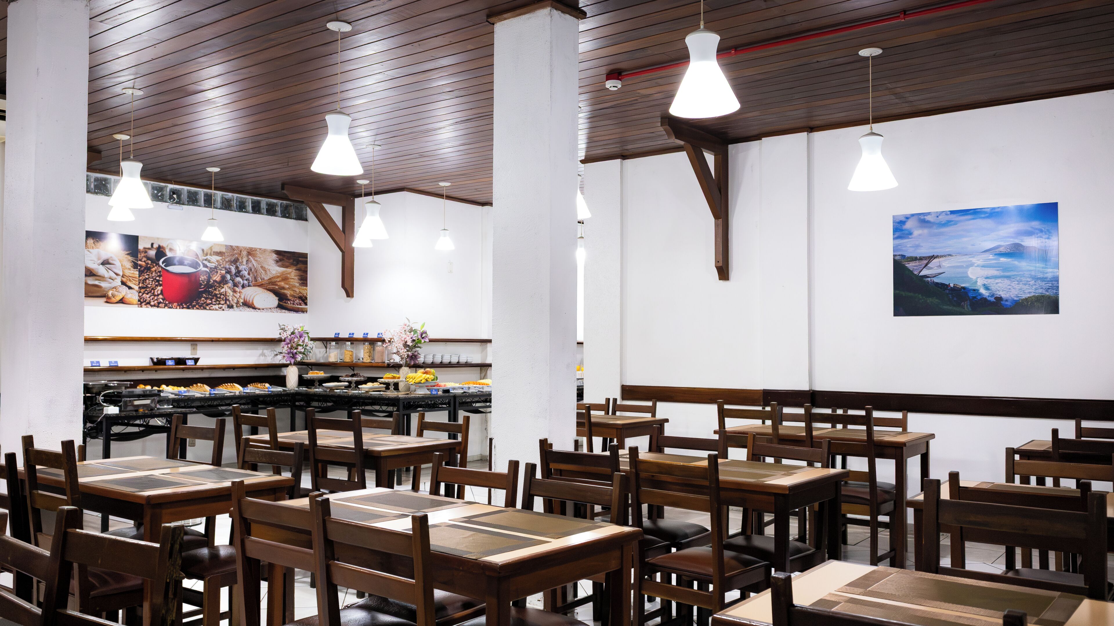 A restaurant interior with wooden tables and chairs, pendant lighting, and wall art.