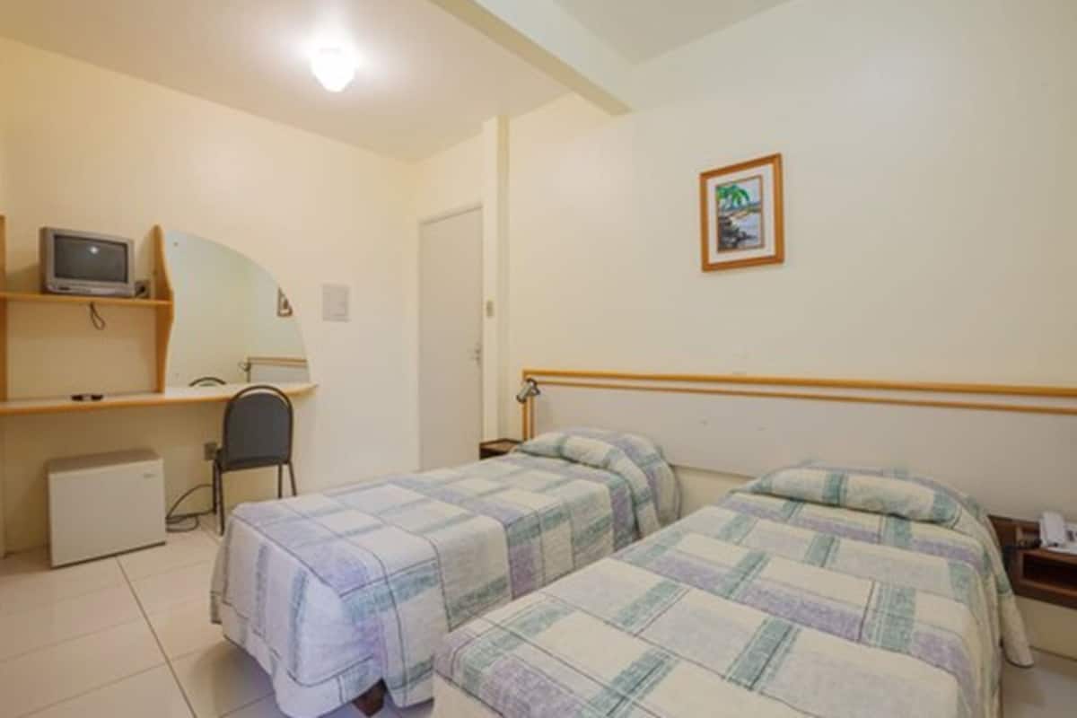 A bedroom with two beds, a desk with a computer, a chair, and a small refrigerator.
