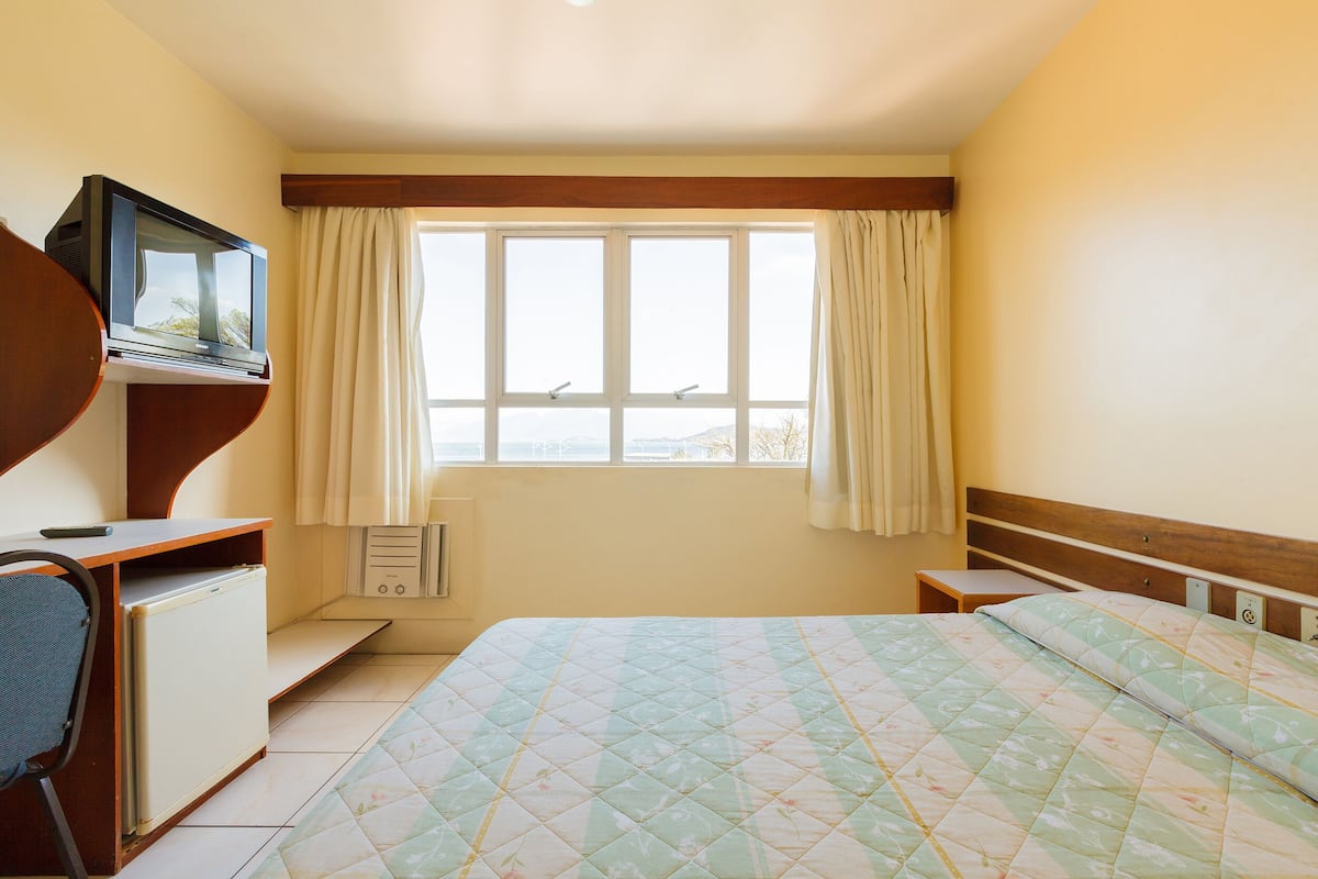 A bedroom with a bed, a desk with a television, a chair, and a window with curtains.
