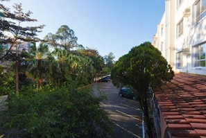 A narrow street with parked cars, lush greenery, and a building with a red-tiled roof. - Tri Hotel Florianópolis (Florianópolis)