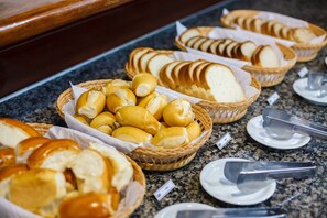 Un buffet proposant une variété de pains et de petits pains, présentés dans des paniers sur un comptoir en granit.