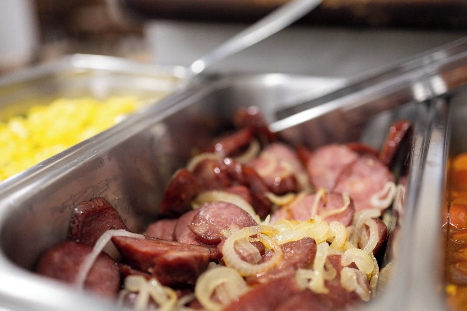 A buffet with various food items, including sliced sausages and onions.