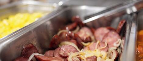 A buffet with various food items, including sliced sausages and onions.