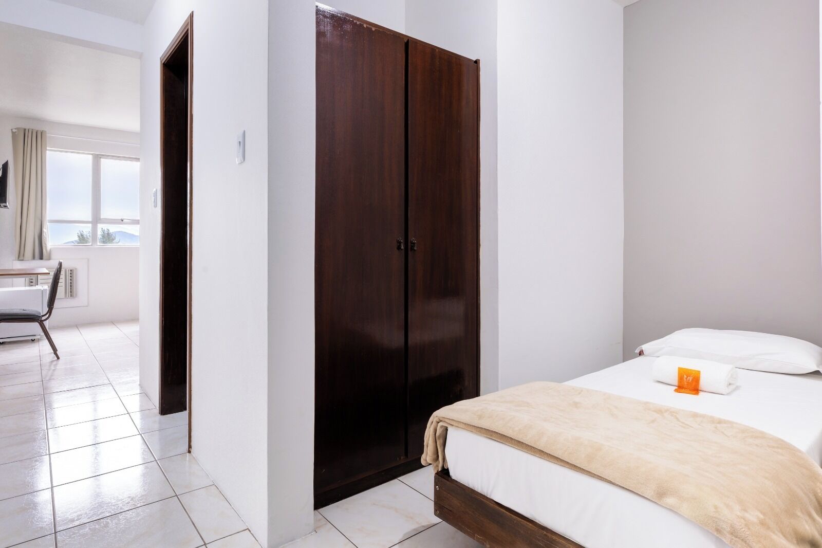A hotel room with a bed, a wardrobe, a desk, and a chair.