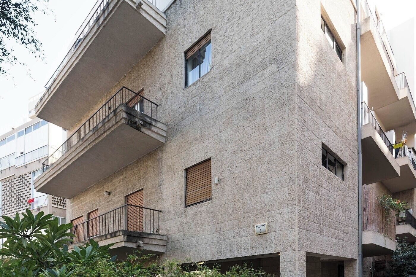 A multi-story building with balconies, a brick facade, and a visible window with shutters.