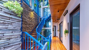 A modern interior with a wooden staircase, stone wall, and a hallway with wooden flooring and glass doors. - Cani Beach House (Da Nang)
