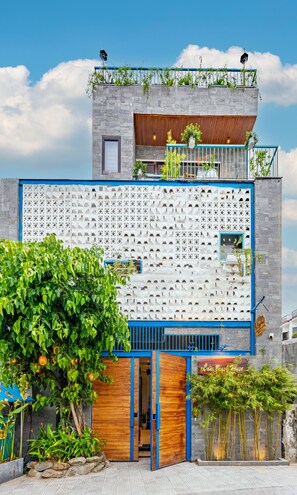 A modern building with a unique geometric facade, a wooden entrance, and a balcony with plants. - Cani Beach House (Da Nang)