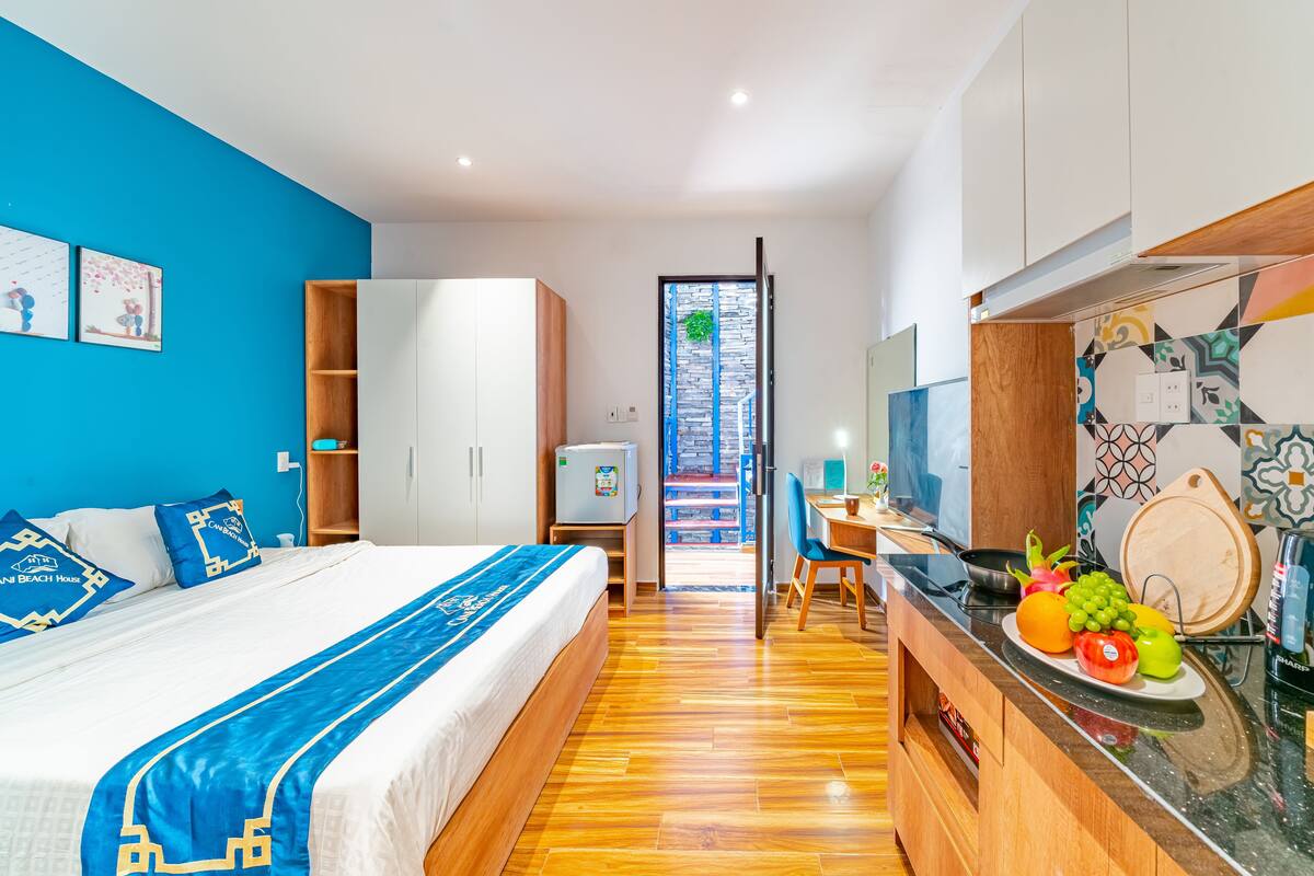 A hotel room with a bed, a desk, a kitchenette, and a view of the outside.
