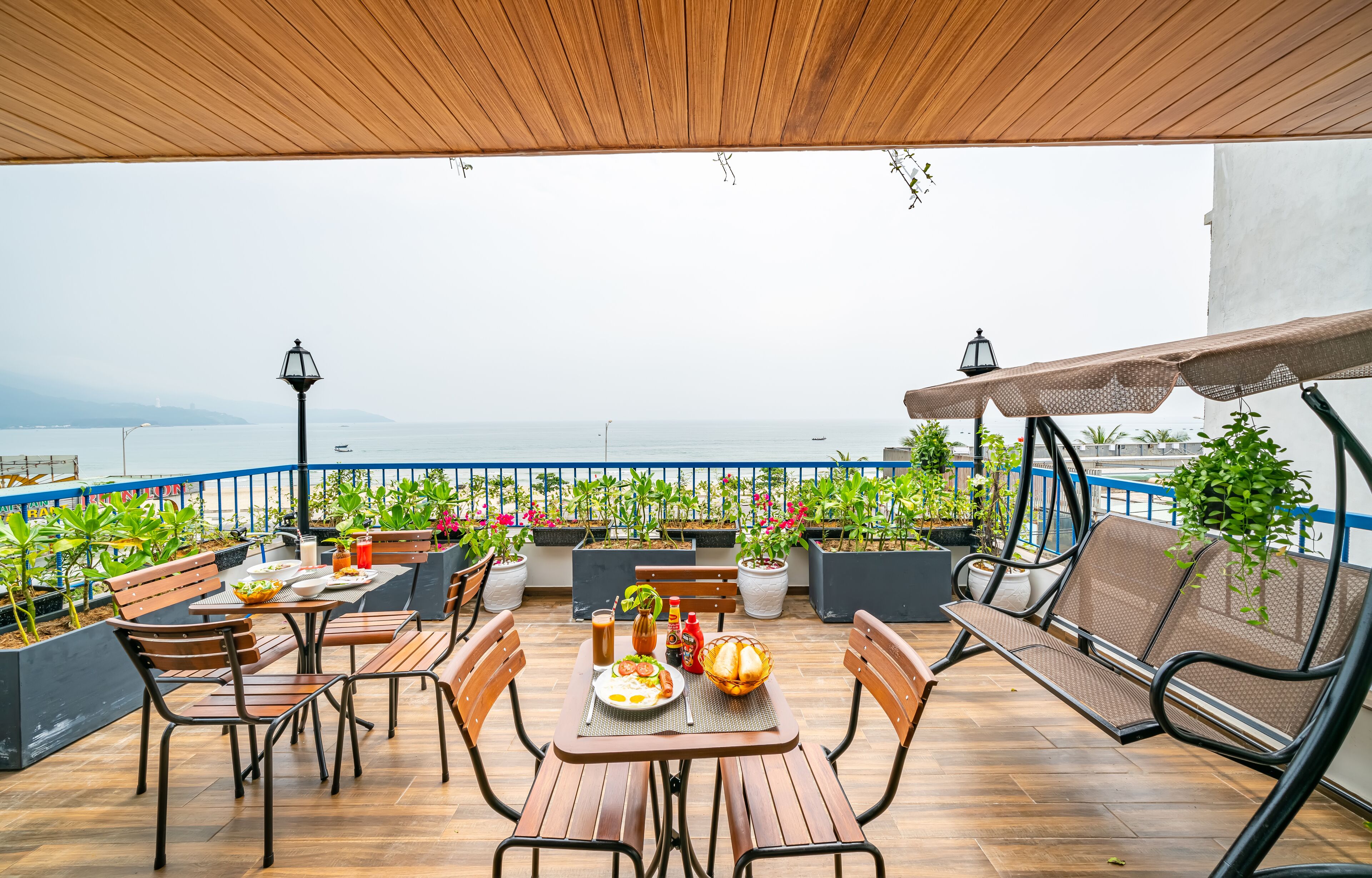 Une terrasse en bois avec des meubles d’extérieur, des plantes en pot et une vue sur la mer.