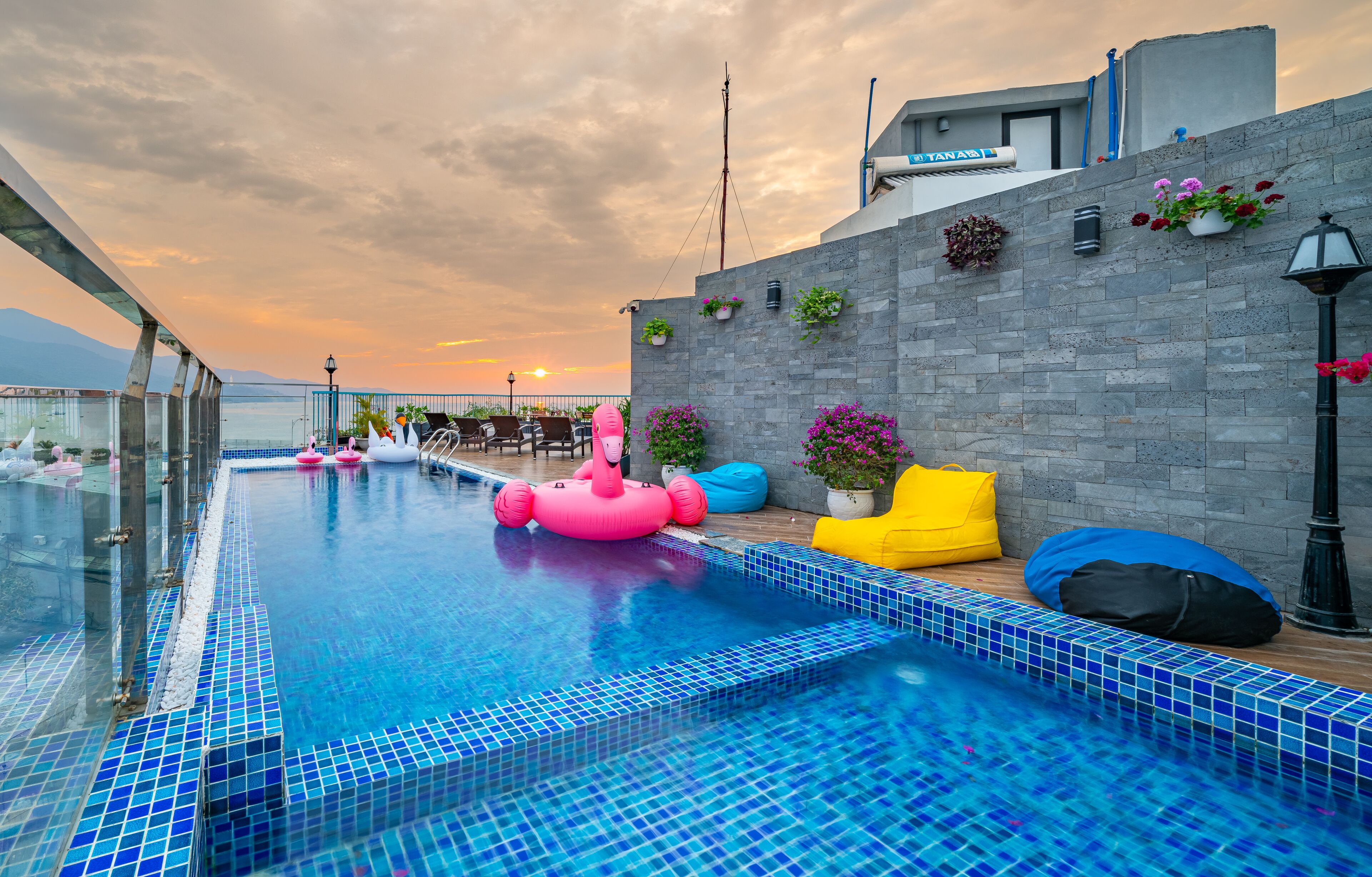 A rooftop swimming pool with a glass barrier, blue-tiled edge, and colorful cushions.