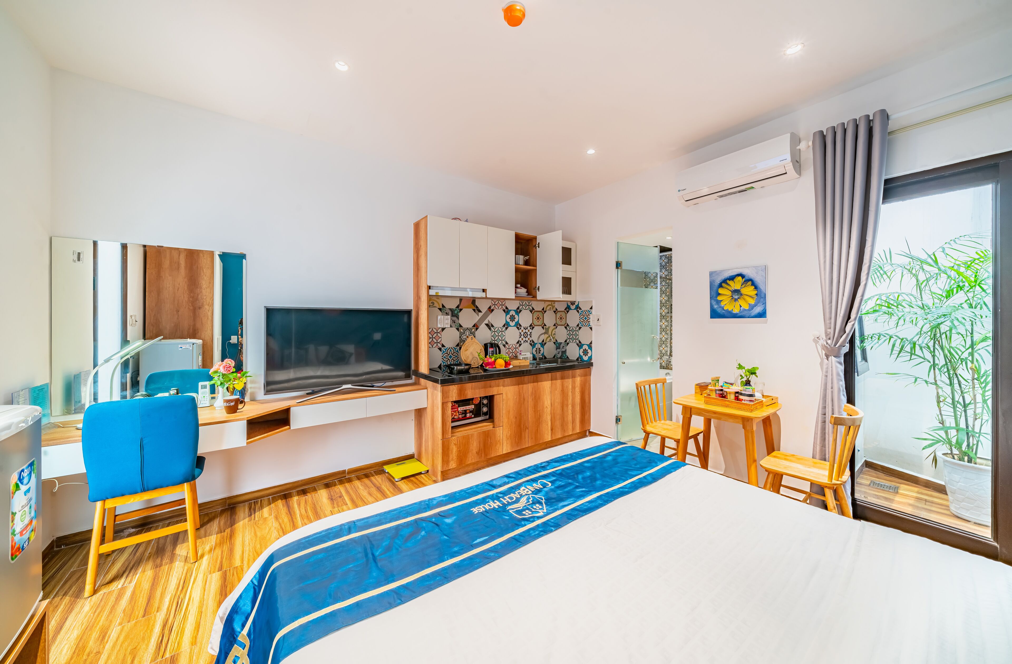 A modern hotel room with a bed, a desk, a kitchenette, and a dining area.