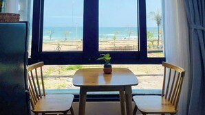 Una habitación con un ventanal grande que da a una playa, una pequeña mesa con dos sillas y una planta en maceta sobre la mesa.