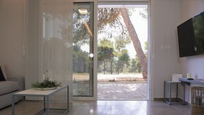 Un salon moderne doté d’une porte-fenêtre coulissante donnant sur une terrasse extérieure, d’un téléviseur à écran plat fixé au mur et d’une petite table d’appoint sur laquelle est posée une bougie.