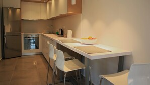 Une cuisine moderne dotée d’un îlot central, de tabourets de bar, d’appareils électroménagers en acier inoxydable et de luminaires suspendus.