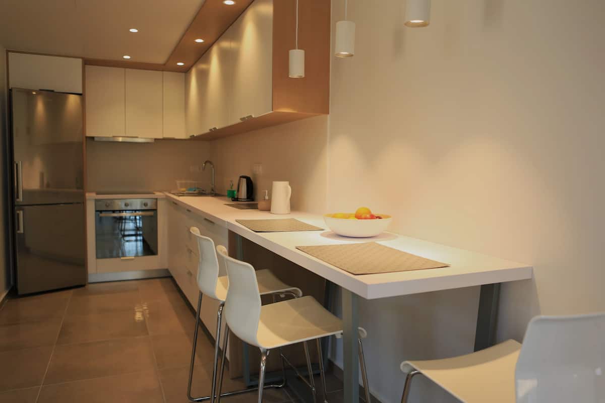 Une cuisine moderne dotée d’un îlot central, de tabourets de bar, d’appareils électroménagers en acier inoxydable et de luminaires suspendus.