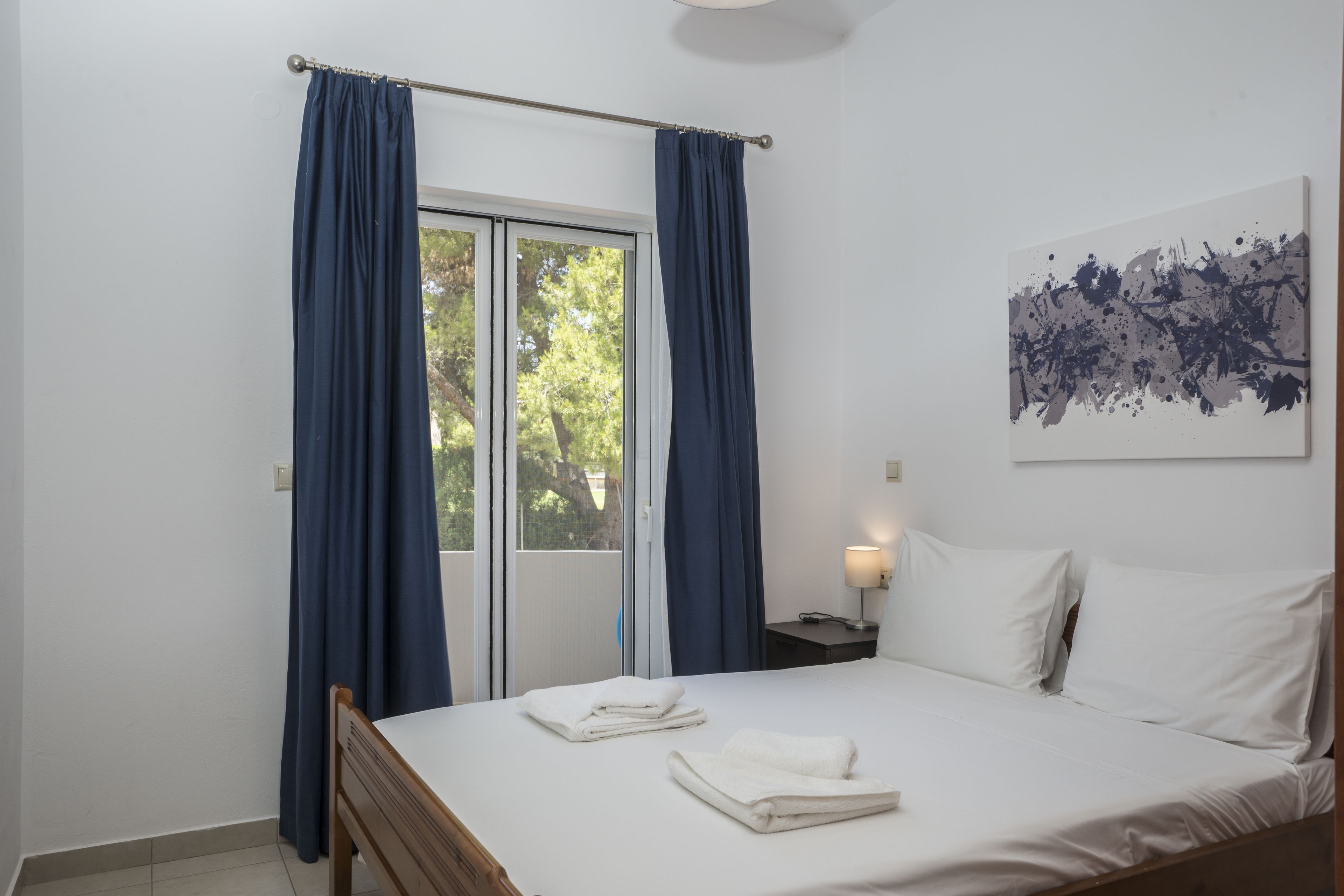 Ein Hotelzimmer mit Bett, Nachttisch, Lampe und einem Fenster mit Vorhängen.
