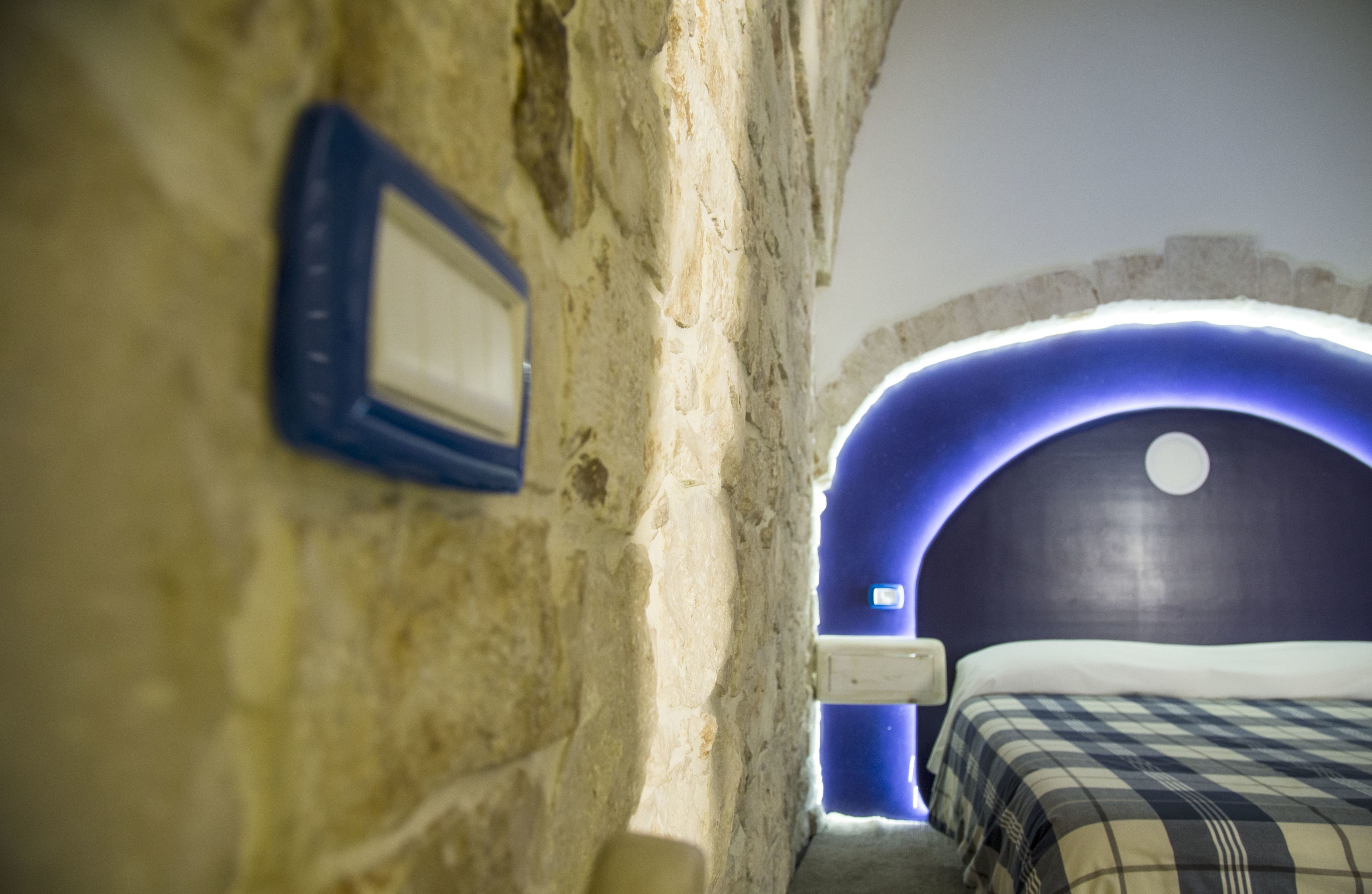 A narrow corridor leading to a room with a checkered bedspread and a blue-lit archway.