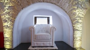 A white armchair in a corner with a stone archway and a window above it. - L'Angolo di Gaudì (Putignano)