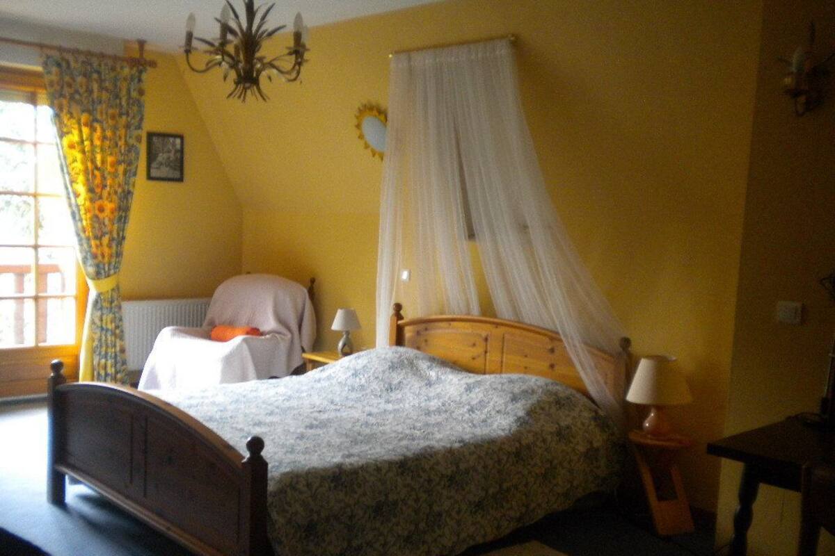 Un dormitorio con cama, mesitas de noche, una ventana con cortinas, una lámpara de araña y un adorno en la pared.