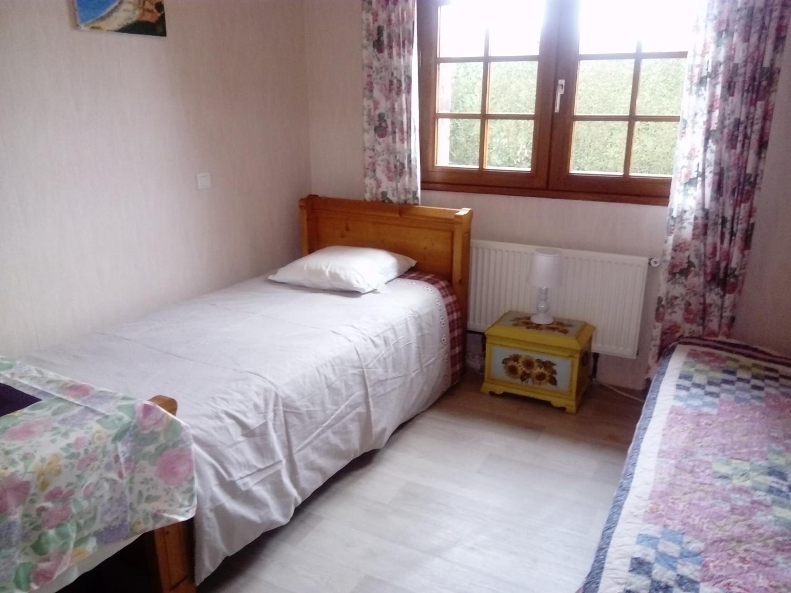 Un dormitorio pequeño con una cama individual, una mesita de noche, una ventana con cortinas y un radiador.
