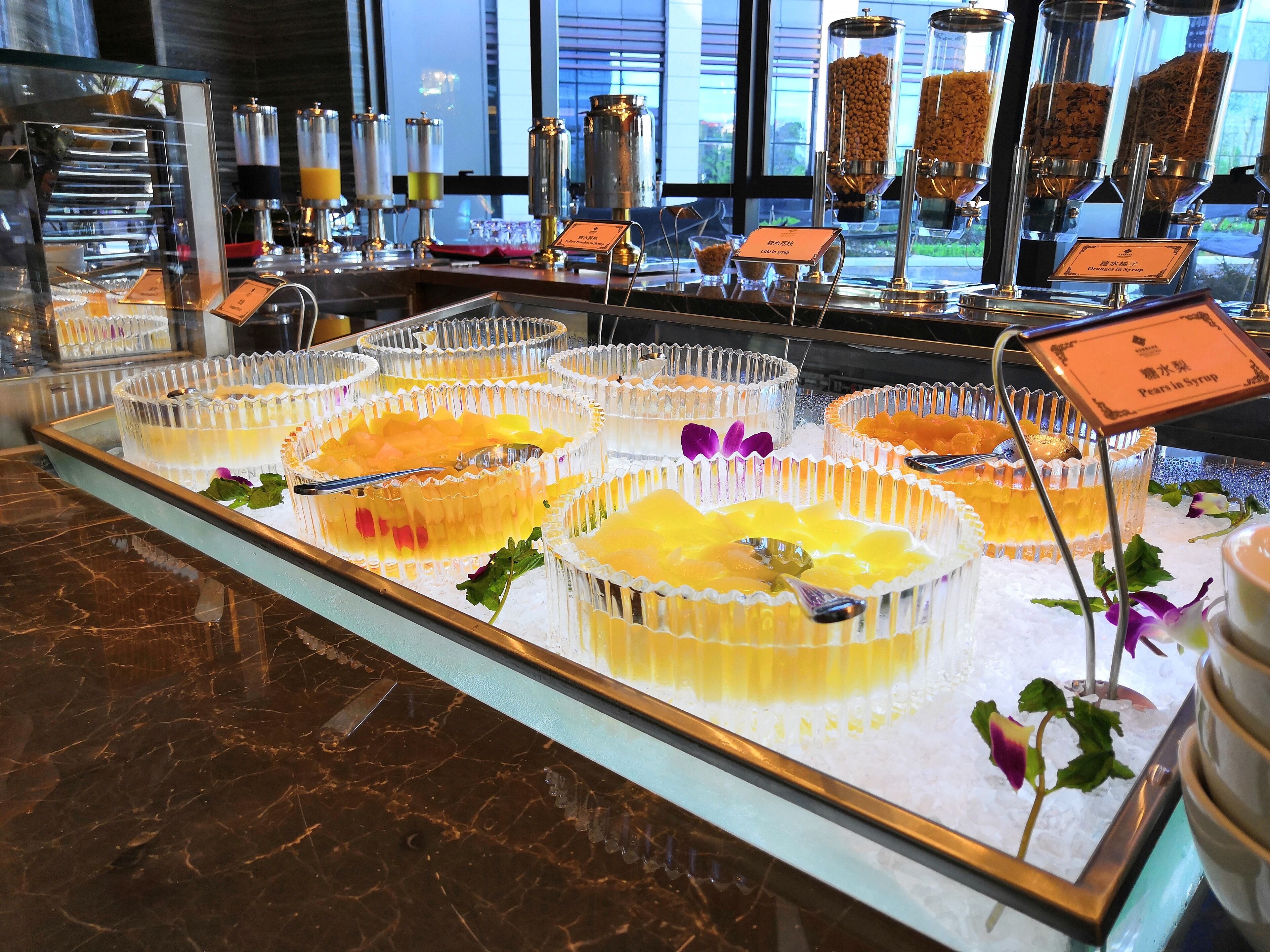 Un présentoir de desserts avec divers mets à base de fruits présentés dans des récipients transparents, accompagné d’un panneau indiquant un parfum de poire au sirop.