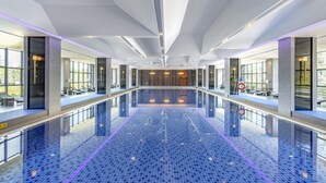 A large indoor swimming pool with a tiled floor, surrounded by glass walls and windows, and a modern ceiling design. - Jinling Grand Hotel Nanchang (Nanchang)