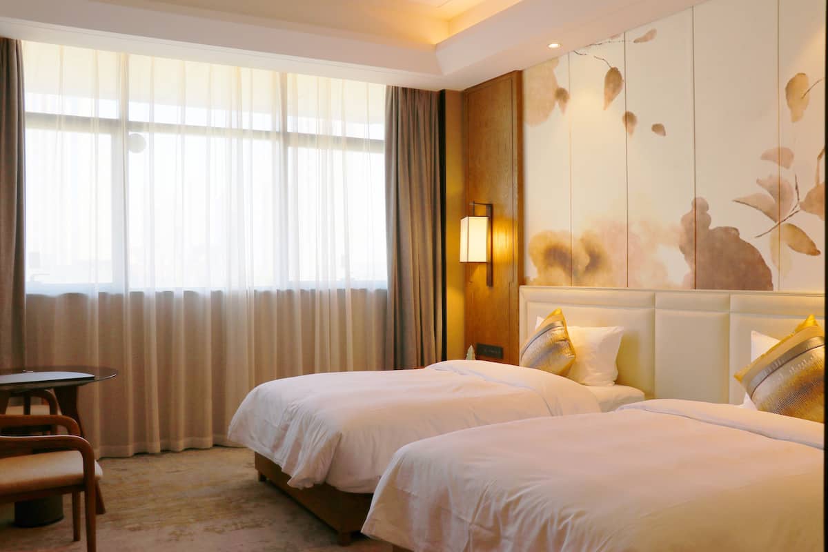 A hotel room with two beds, a table, and a chair.