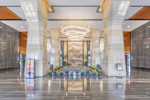Eine großzügige Lobby mit einer zentralen Kunstinstallation, einer Rezeption und Zimmerpflanzen.