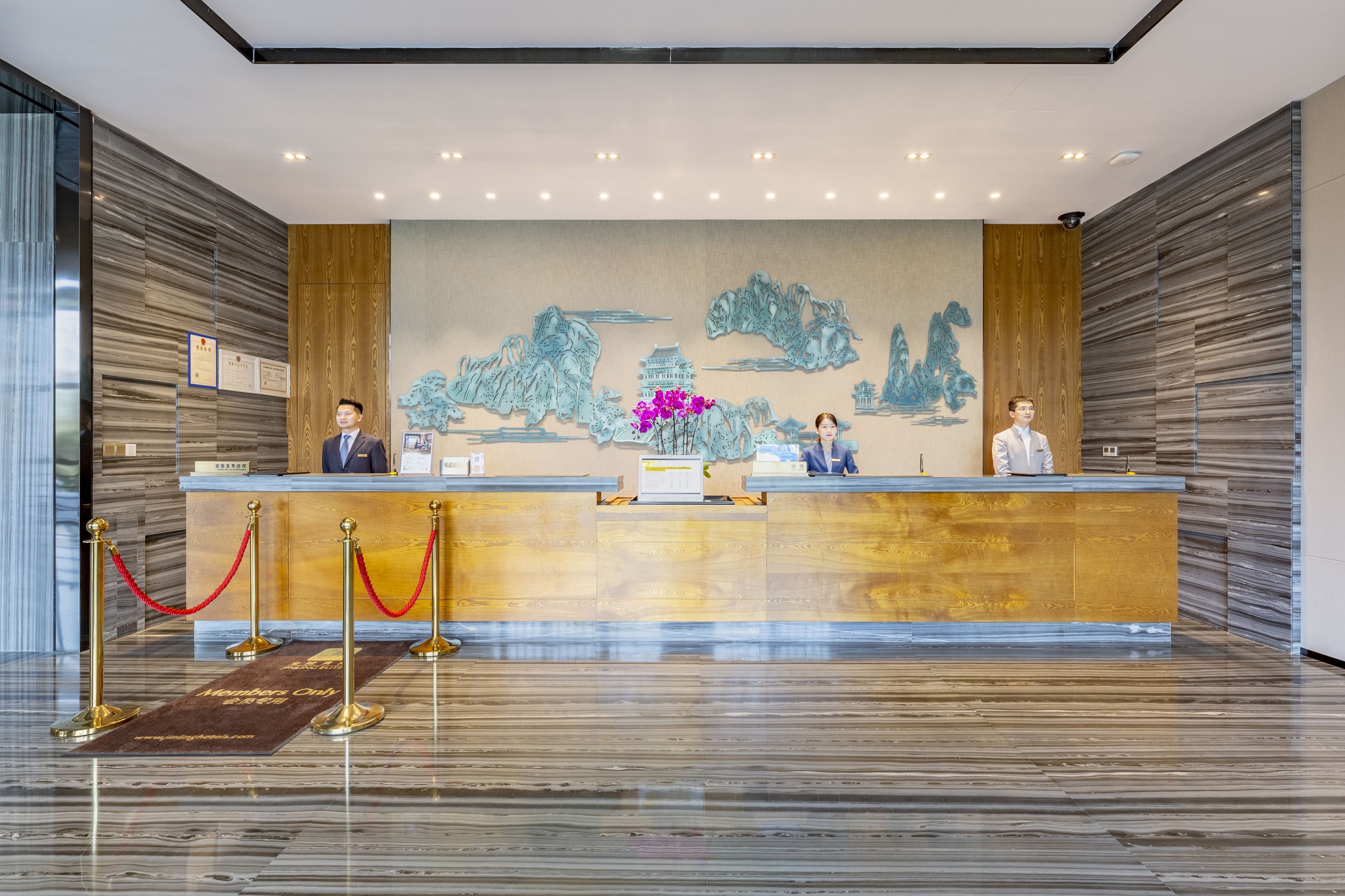 A reception area with a wooden reception desk, two staff members, and a decorative wall mural.