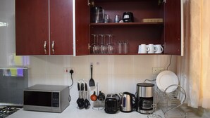 Een keuken met een magnetron, broodrooster, waterkoker, koffiezetapparaat en diverse keukengerei.