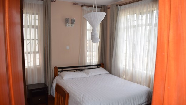Een enkel bed met houten frame en witte lakens in een kamer met beige wanden en een houten vloer.