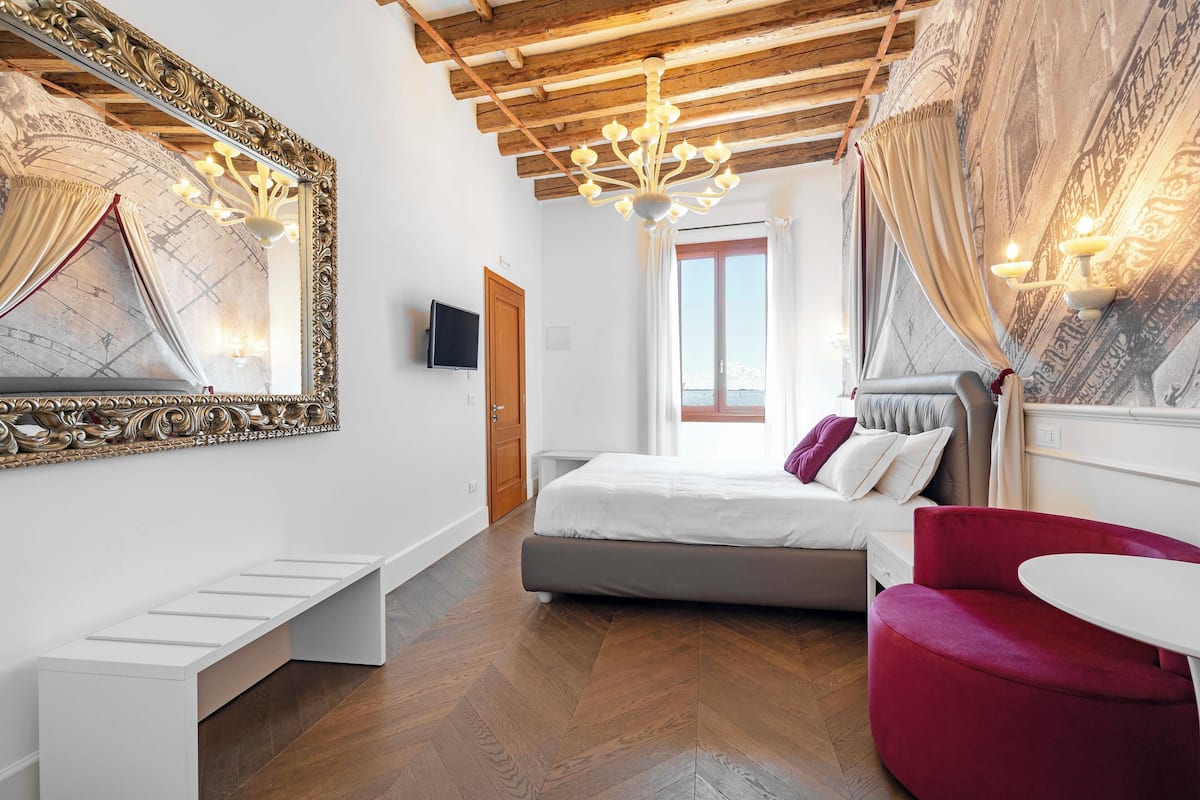 Une chambre à coucher moderne avec un lit, un fauteuil rouge, une table blanche et un grand miroir.