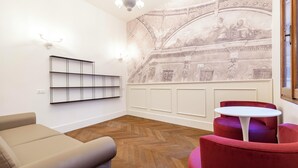 Un interior moderno con piso de madera en patrón de espiga, un sofá beige, una silla roja, una mesa blanca y un mural decorativo.