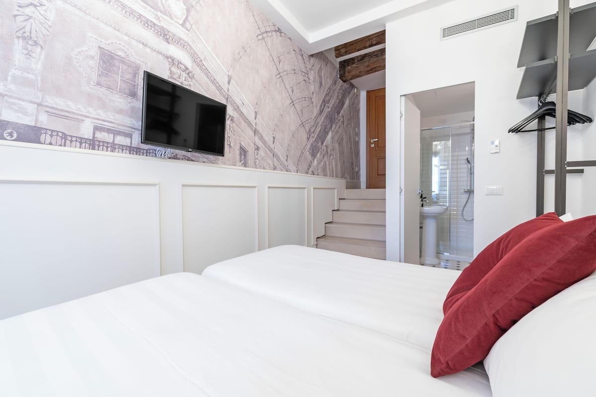 Une chambre à coucher avec un lit, un oreiller rouge, un téléviseur fixé au mur et un escalier menant à une salle de bain.