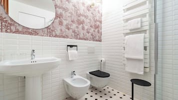 A bathroom with a white sink, bidet, and toilet, a mirror, and a towel rack.