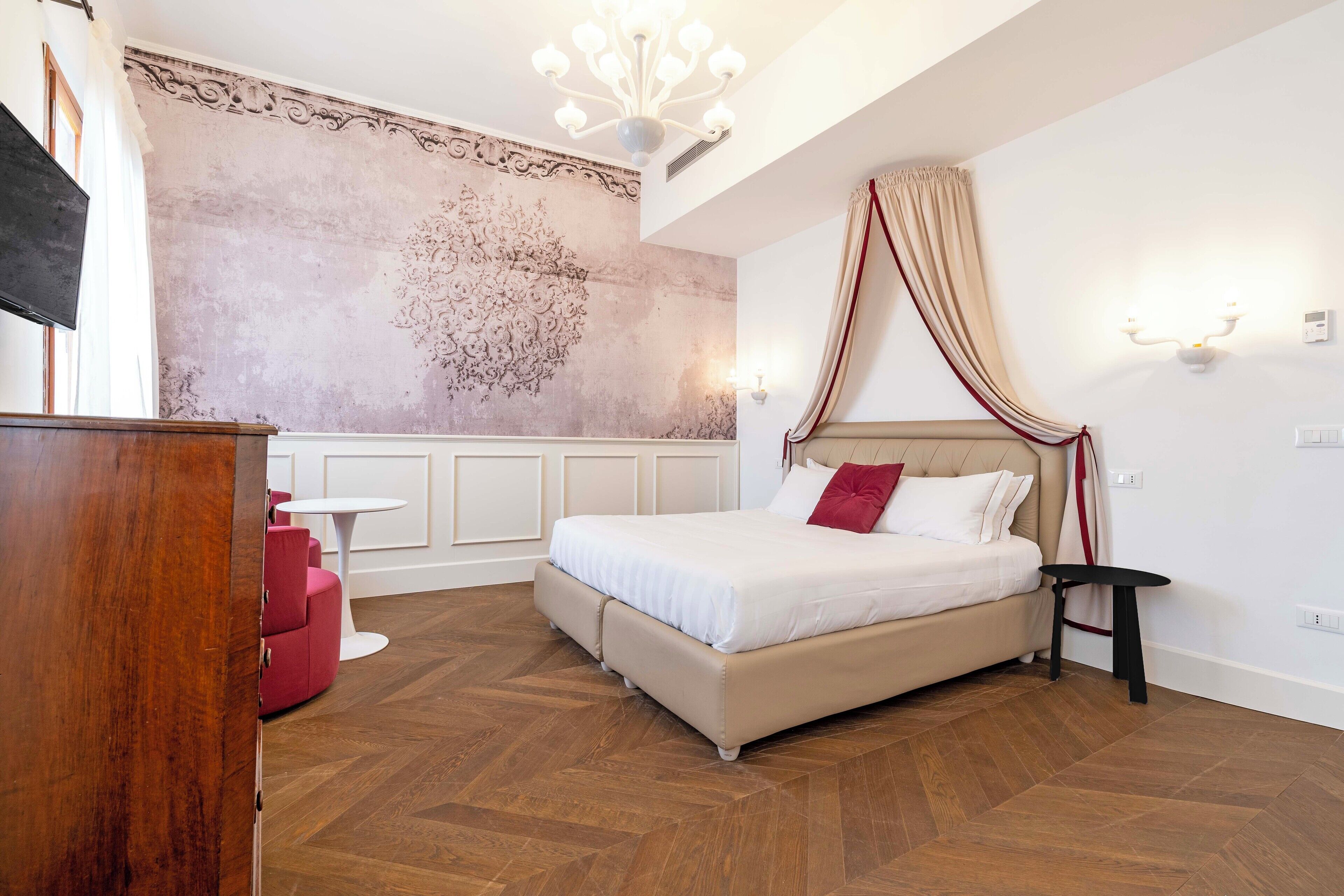 Un dormitorio con una cama grande, una mesita pequeña, una silla roja y un adorno en la pared.