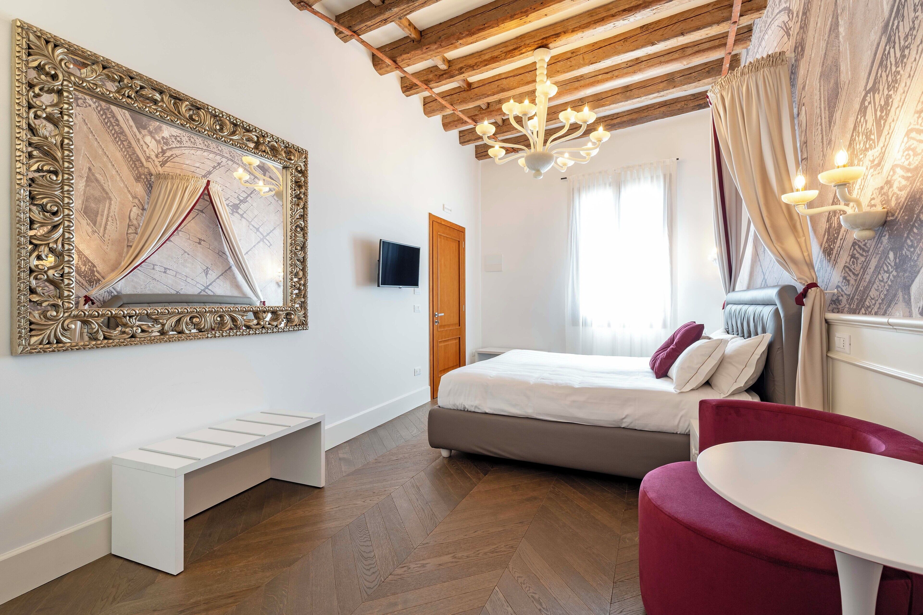 A modern bedroom with a large mirror, a bed, a bench, a table, and a TV.